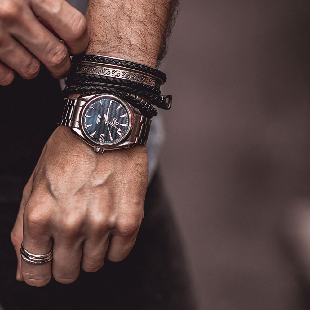 Hand wearing a wristwatch with multiple bracelets on a blurred background