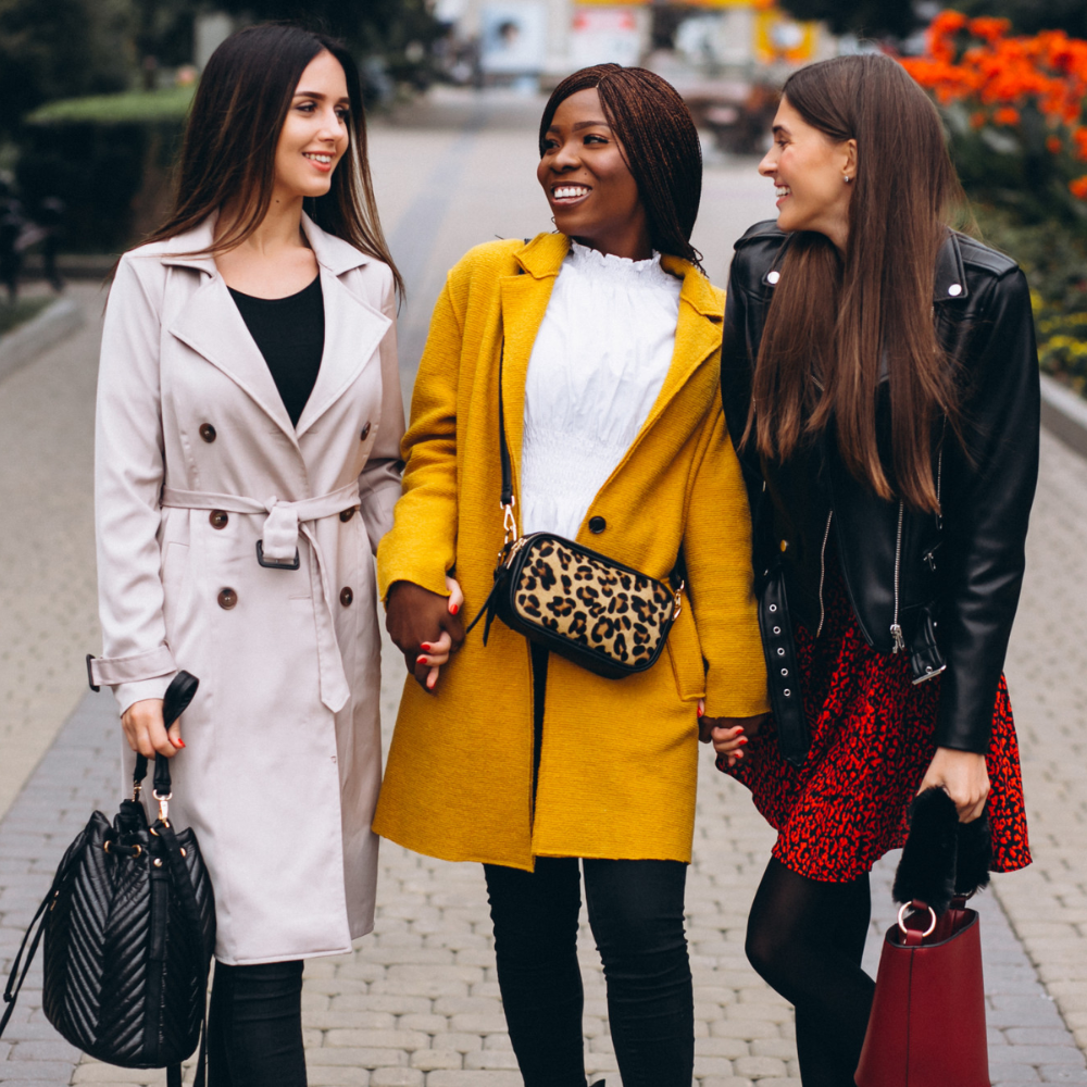 Three women walking together on a sidewalk, smiling and holding hands.