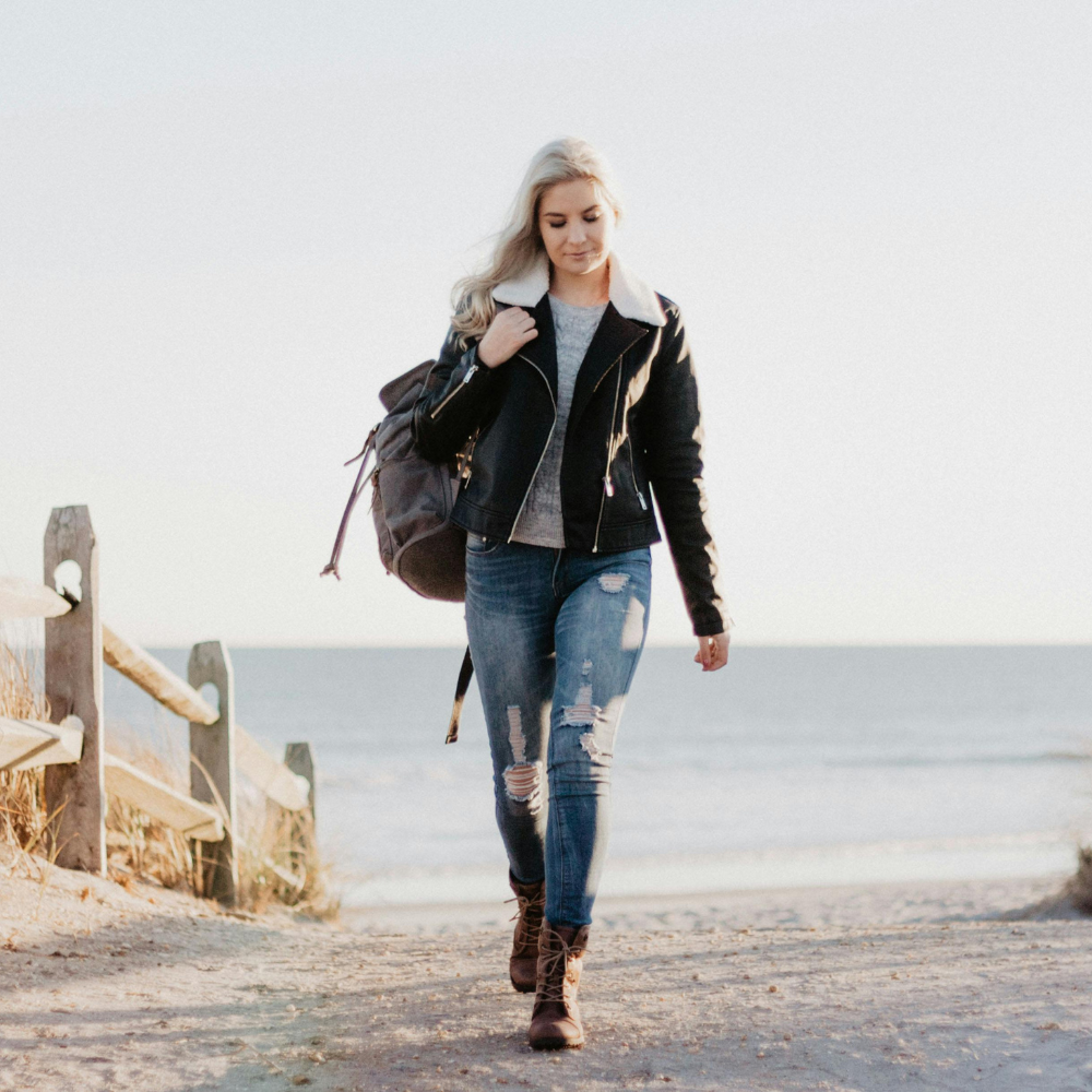 Woman walking on a beach path with a backpack